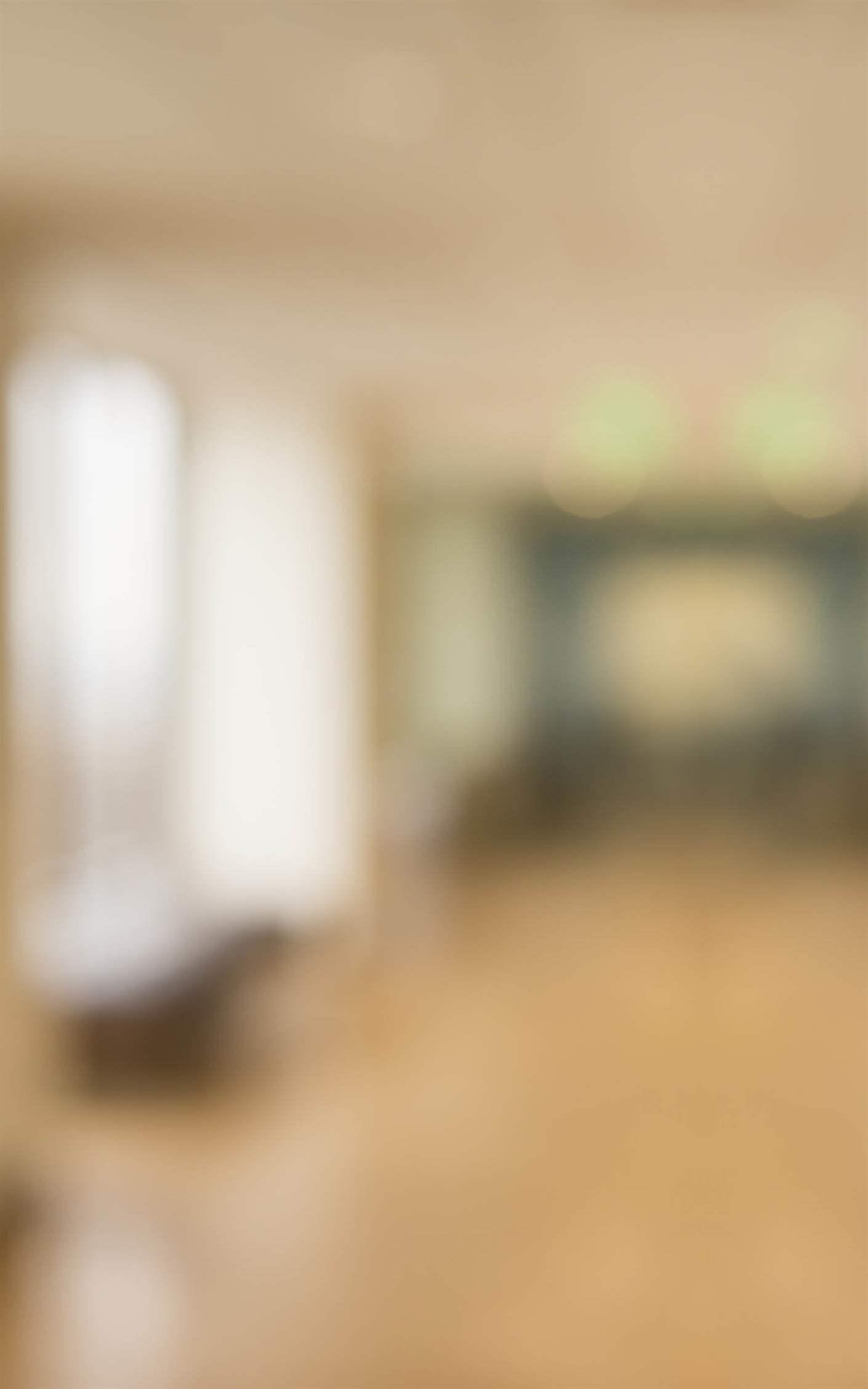 A blurry panoramic photograph of an office corridor with overhead lighting